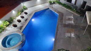 A rectangular swimming pool with a hot tub, surrounded by lounge chairs and potted plants.