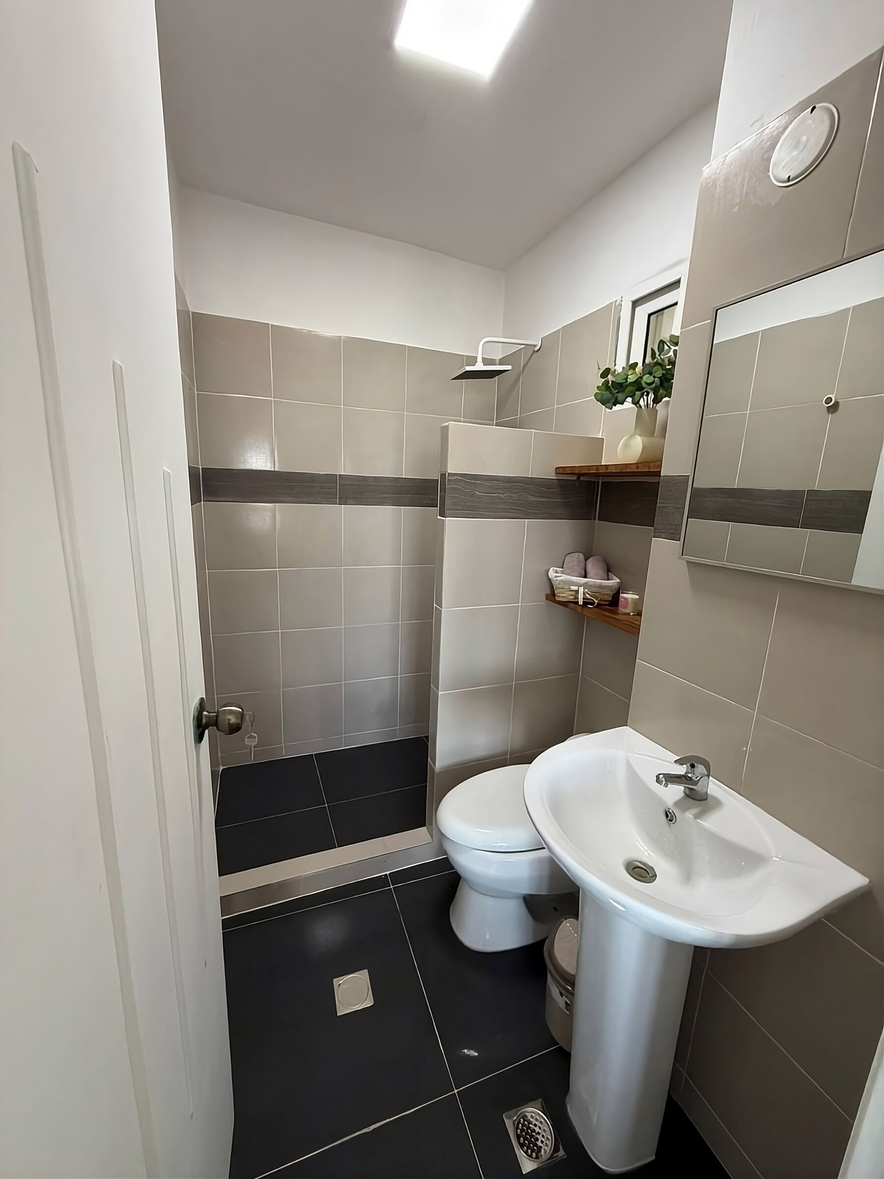 Une salle de bain équipée d’une douche, de toilettes et d’un lavabo, avec des murs carrelés et un sol noir.