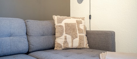 A corner of a room with a grey sofa, a patterned throw pillow, and a black floor lamp.