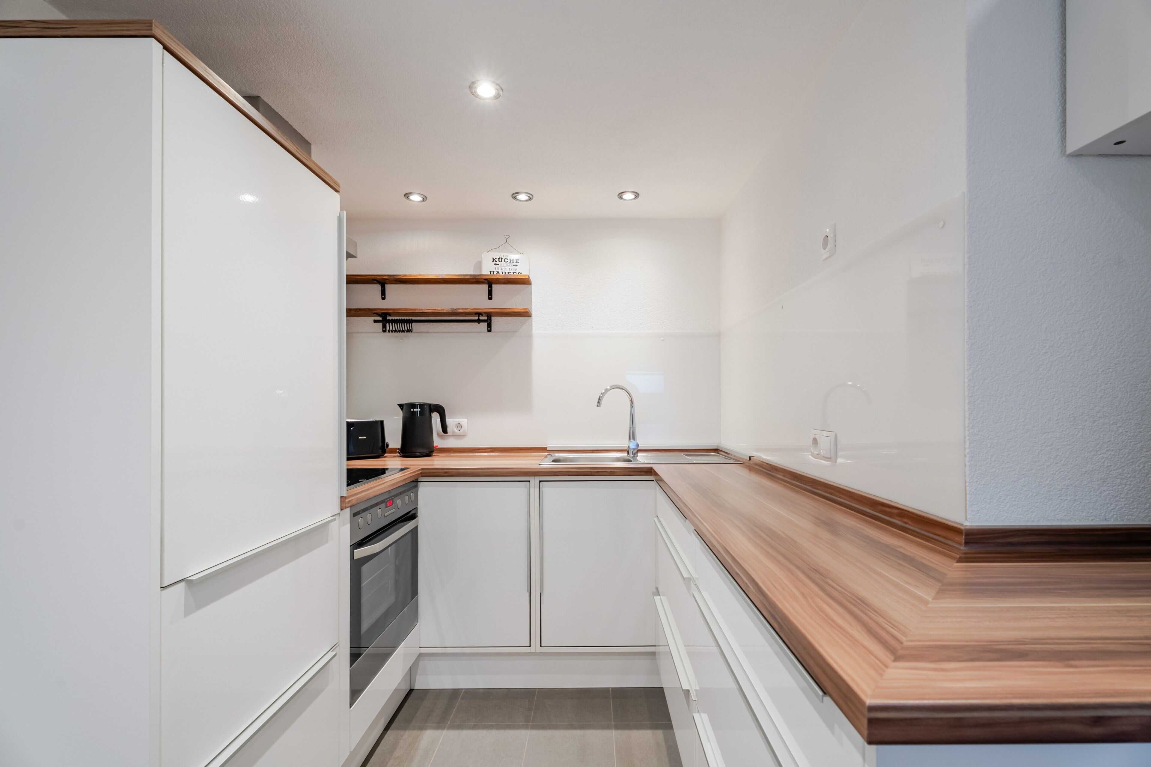 Eine moderne Küche mit weißen Schränken, einer Holz Arbeitsplatte und einem eingebauten Backofen.