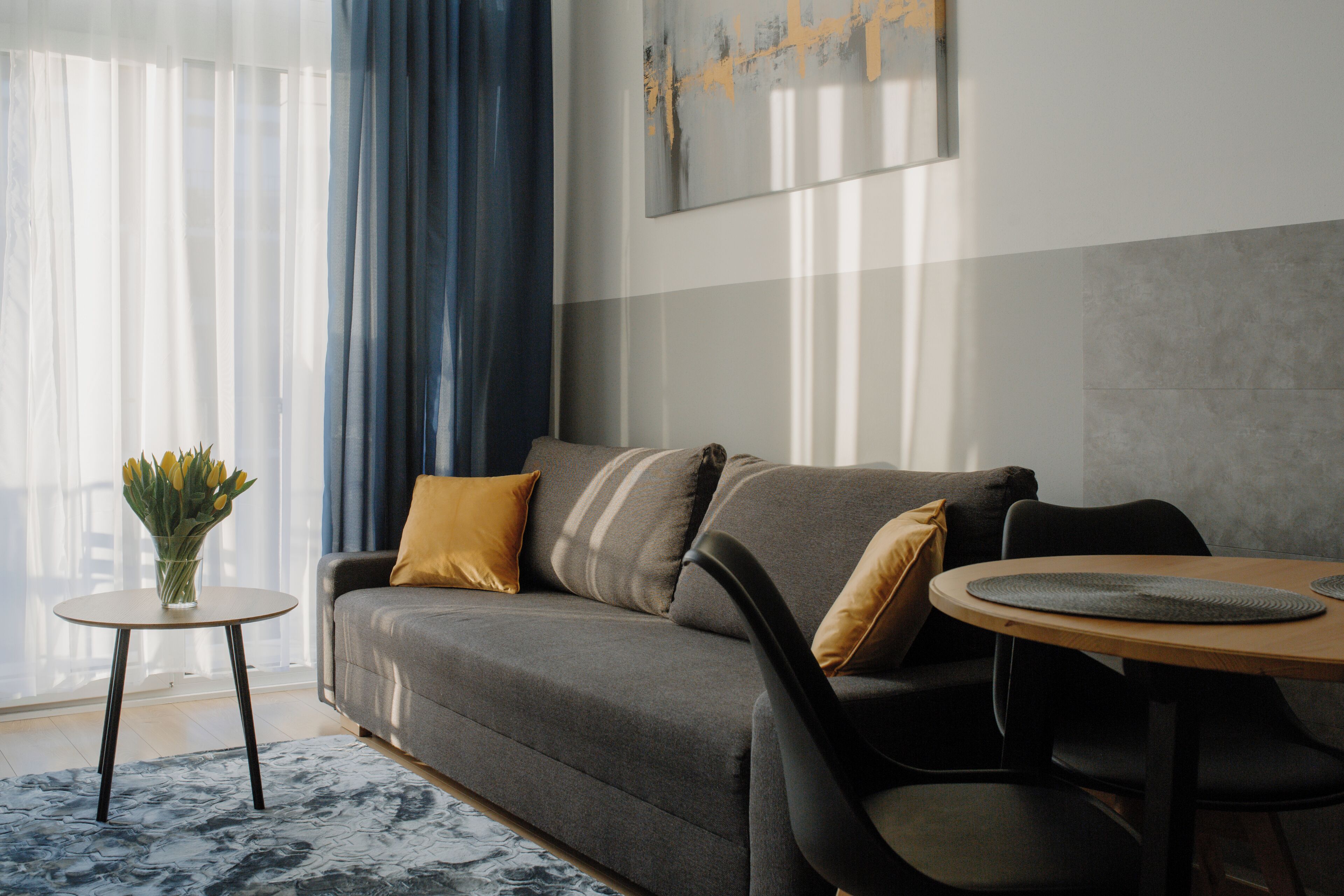 A modern living room with a grey sofa, a small round table, and a vase of yellow flowers.