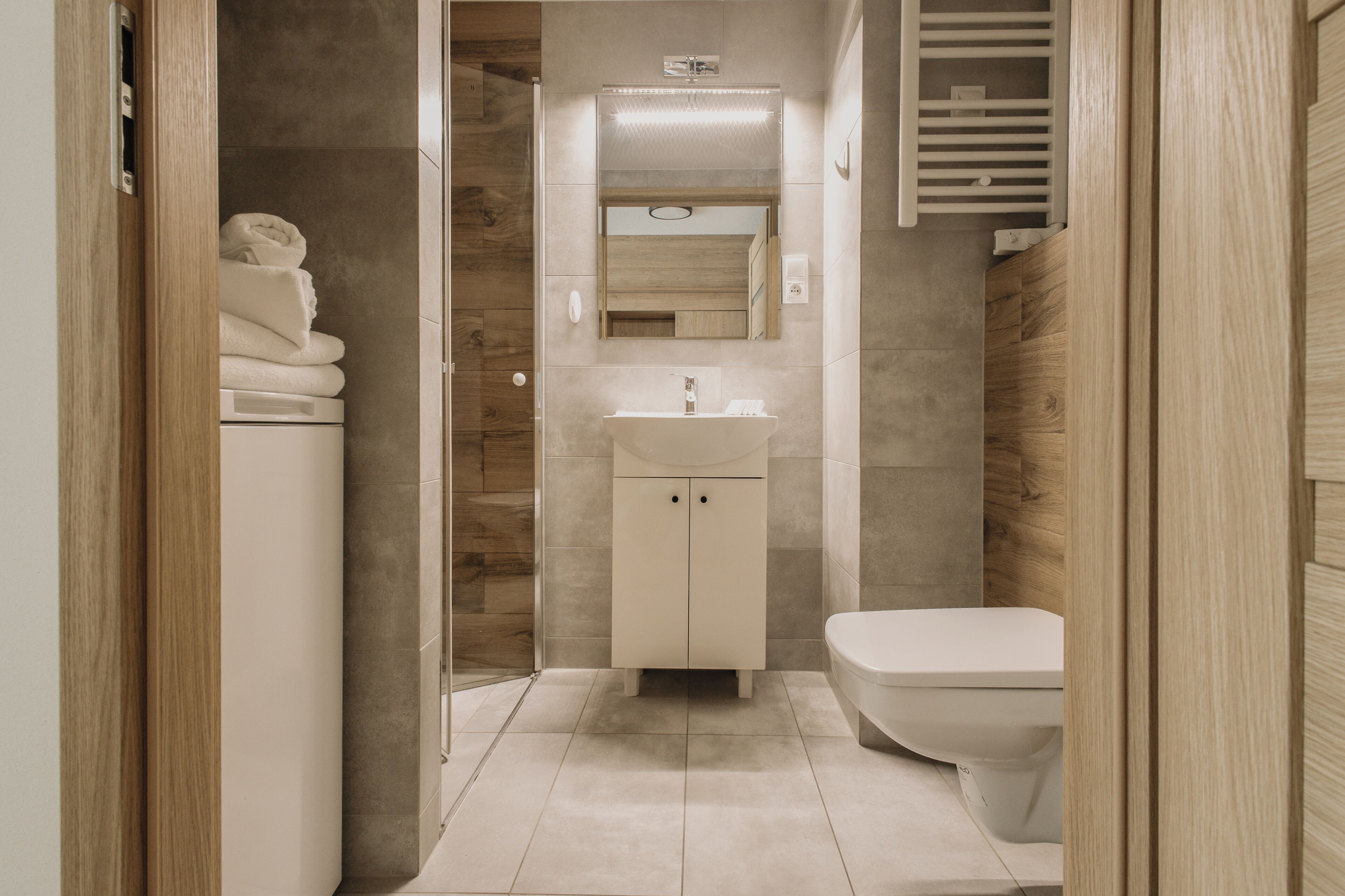 A modern bathroom with a shower, toilet, and sink, featuring wooden paneling and a mirror above the sink.