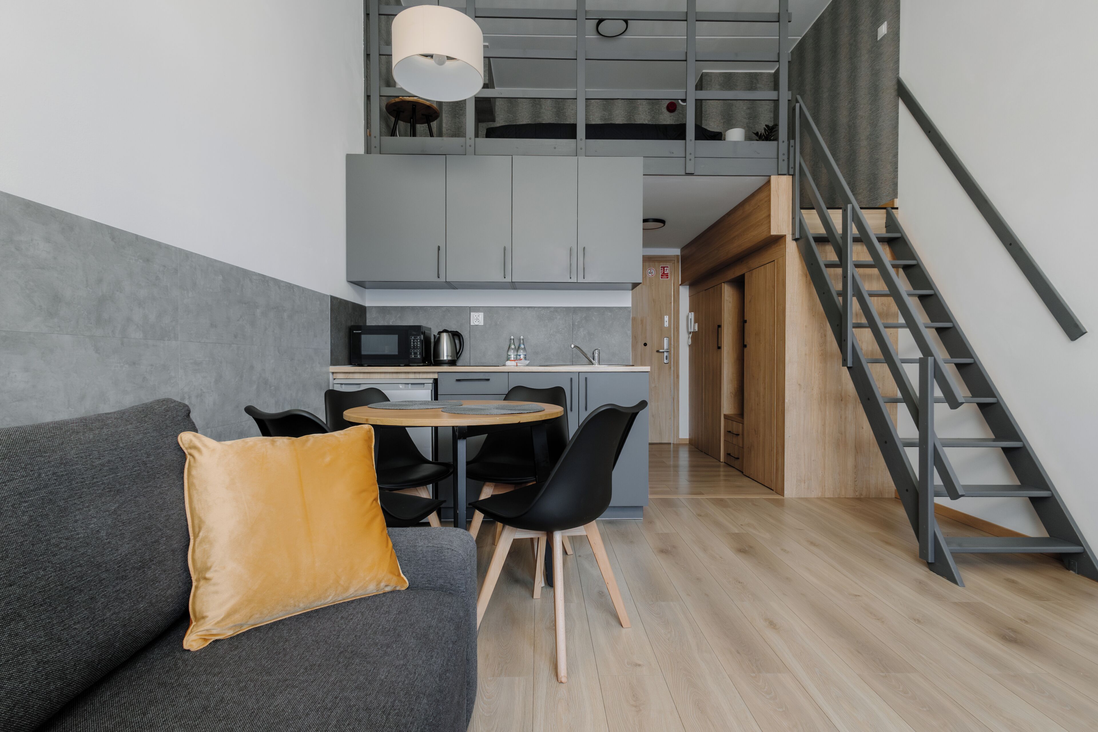 Een moderne keuken met grijze kastjes, een zithoek met een ronde tafel en stoelen, en een trap met een metalen leuning.