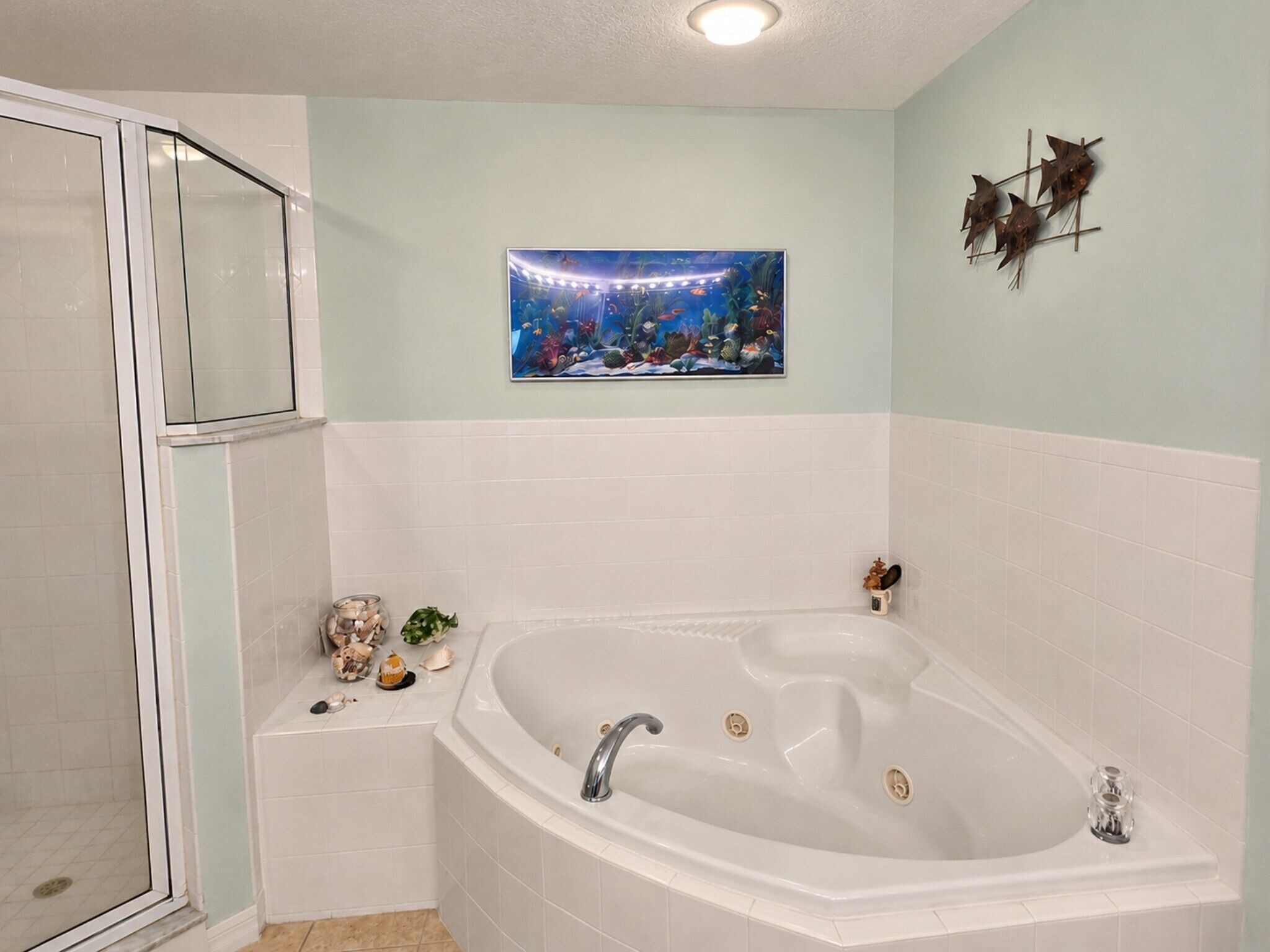 A bathroom with a bathtub, a glass shower enclosure, and a wall-mounted artwork depicting an underwater scene.