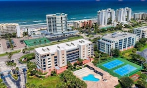 Ein Hochhotel mit mehreren Etagen, einem Schwimmbad, Tennisplätzen und Blick auf den Strand.