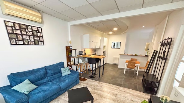 A living room with a blue sofa, a black coffee table, and a dining area with a wooden table and chairs. - Cozy 1-bedroom apartment with AC and a jetted tub in gorgeous Strasbourg (Strasbourg)