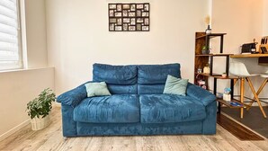 A blue sofa in a room with a wooden floor, a wall-mounted picture frame, and a plant. - Cozy 1-bedroom apartment with AC and a jetted tub in gorgeous Strasbourg (Strasbourg)