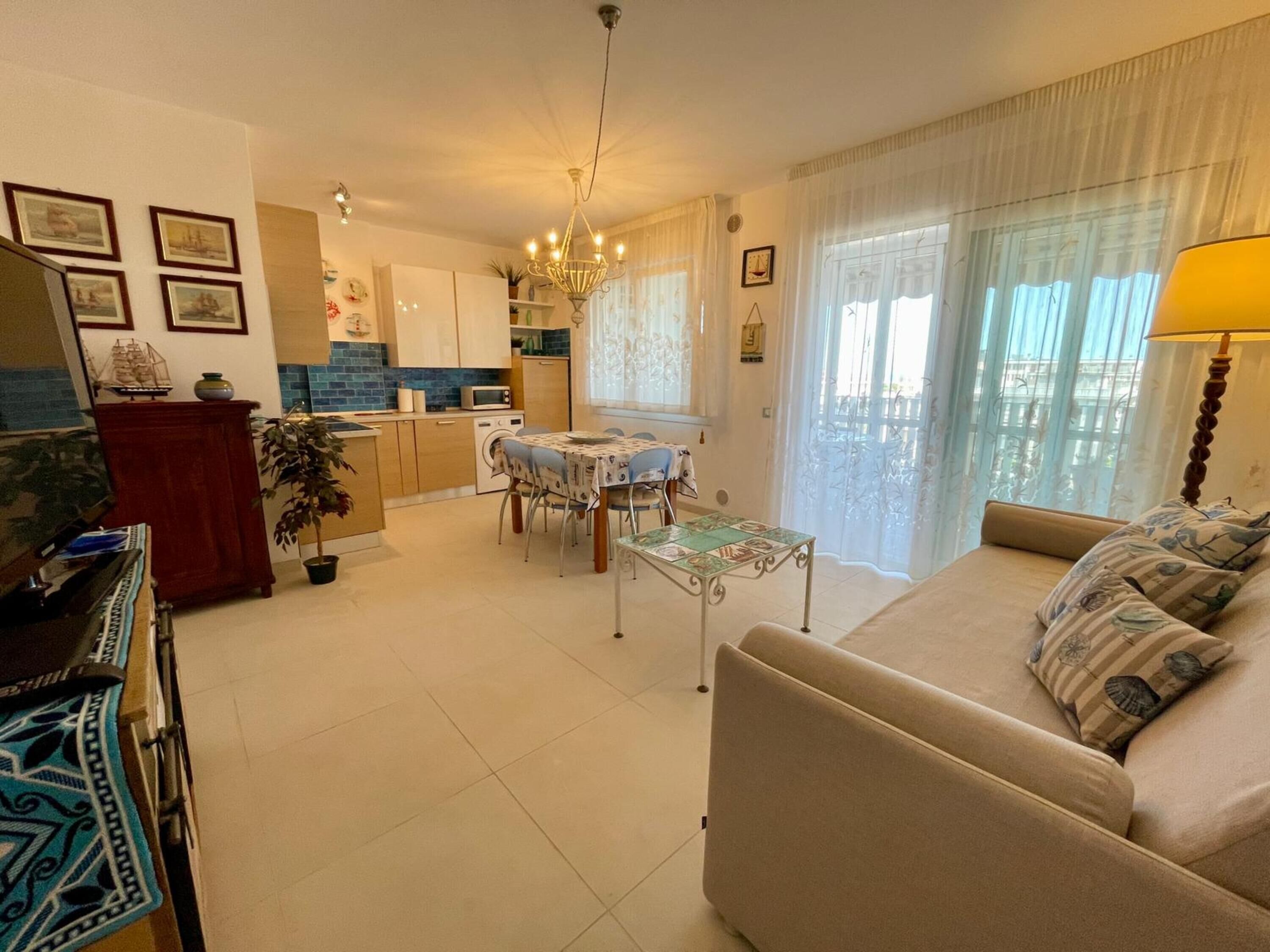 A living room with a sofa, a dining table with chairs, a kitchen area with cabinets and a microwave, and a chandelier.