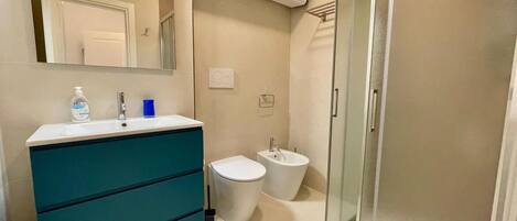 A bathroom with a sink, mirror, cabinet, bidet, and glass shower enclosure.