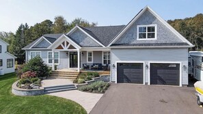 A two-story house with a front porch, a garage, and a landscaped yard. - Casa Bonita PEI – Spacious, Relaxing, Dog-Friendly (Stratford)