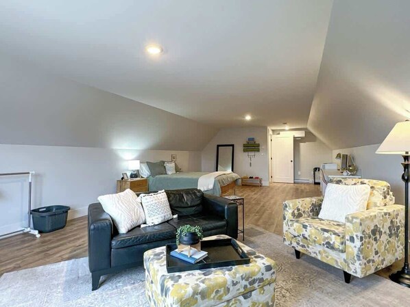 Un espacioso dormitorio tipo loft con una cama grande, una zona de estar con sofá y sillón, y un comedor con mesa y sillas.