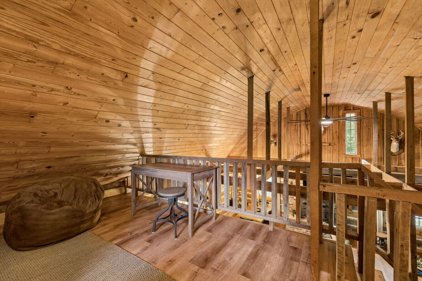 A wooden interior with a table and bench, a wooden railing, and a mounted animal head.