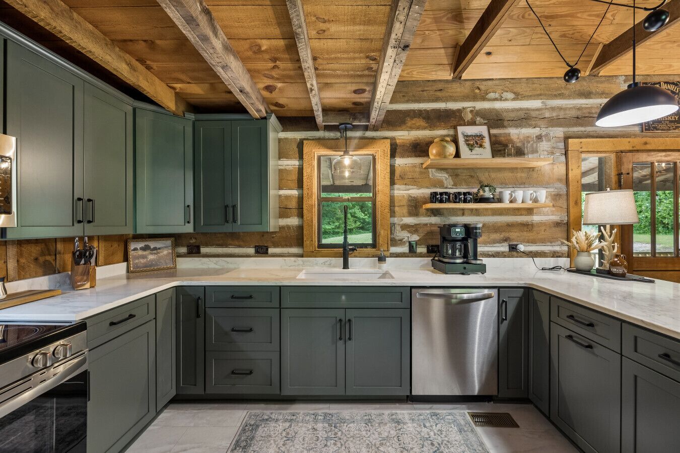 A rustic kitchen with wooden beams, green cabinets, a stainless steel dishwasher, and a coffee maker.