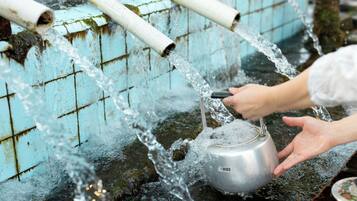 A person filling a kettle from a water source with visible pipes and a tiled wall.