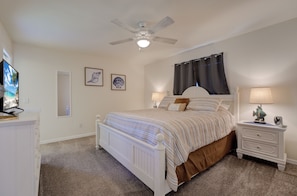 Ein Schlafzimmer mit Bett, Nachttischen, Deckenventilator und Wandbildern.
