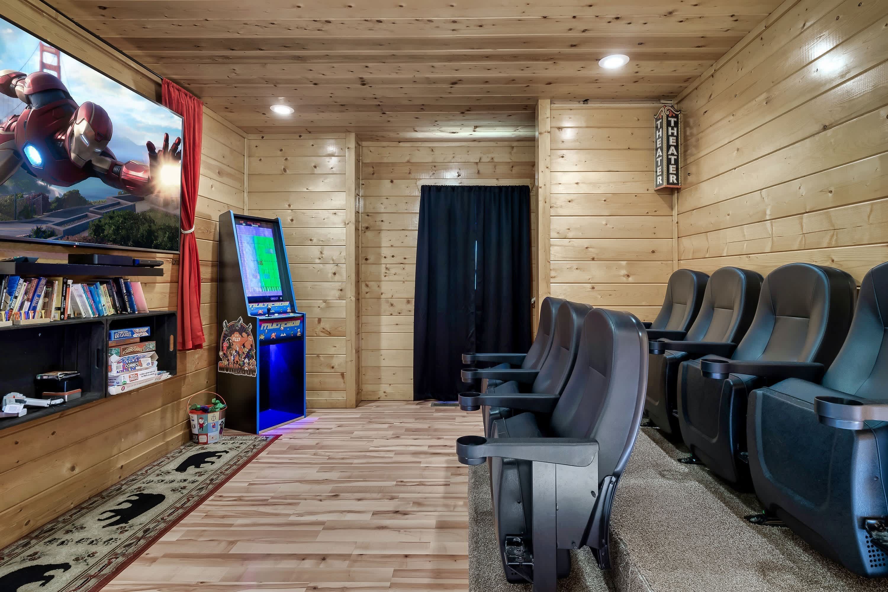 Une salle de cinéma aux murs en bois, dotée d’un écran, d’une console de jeux et de plusieurs rangées de sièges.