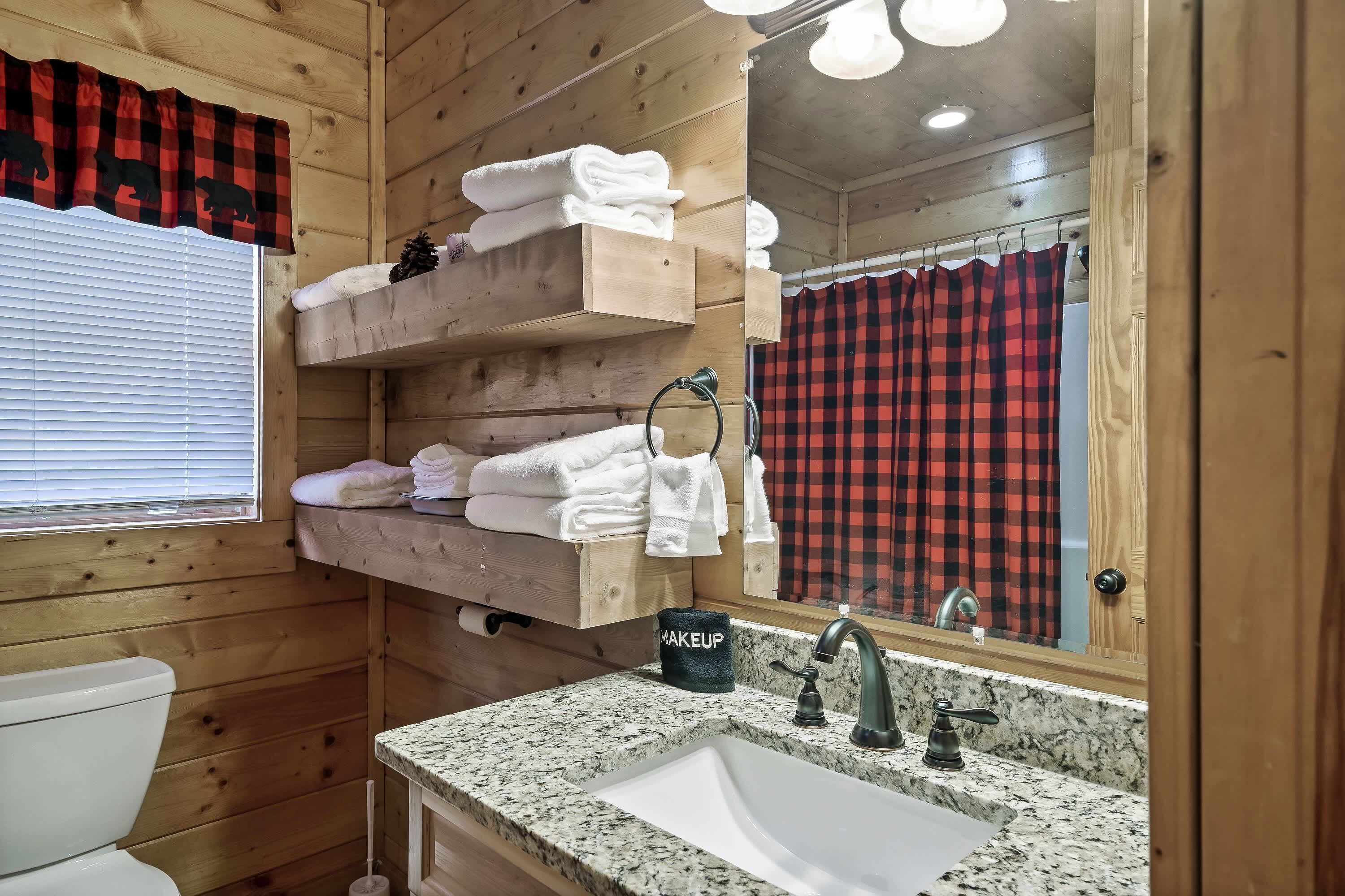 A wooden cabin bathroom with a sink, mirror, towel rack, and a window with blinds.