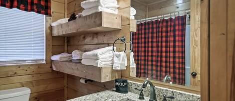 A wooden cabin bathroom with a sink, mirror, towel rack, and a window with blinds.