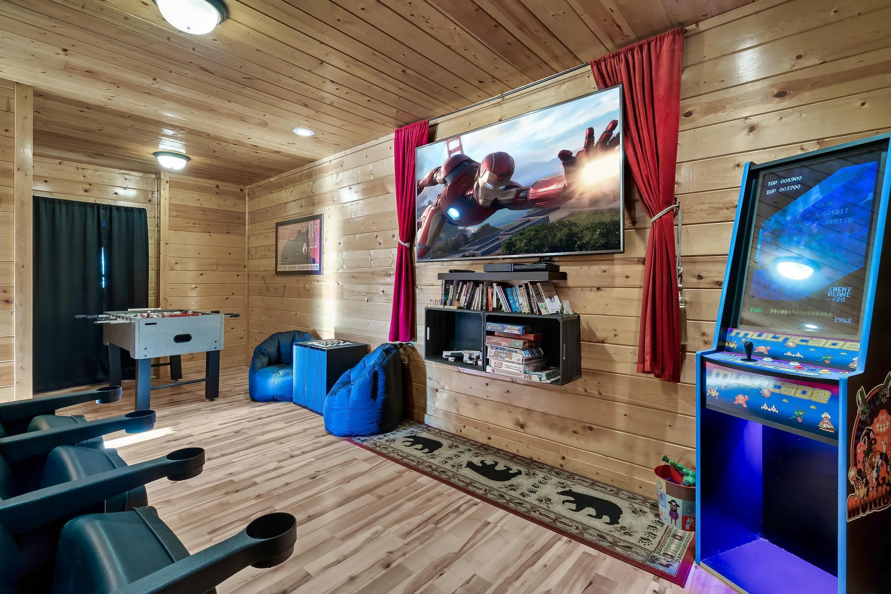 Une pièce aux murs en bois, avec un grand écran de télévision, un baby-foot, un fauteuil-pouf bleu et une machine à pinces.