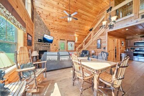 L’intérieur d’une cabane en rondins comprend un coin repas, une cuisine, une cheminée et un téléviseur.