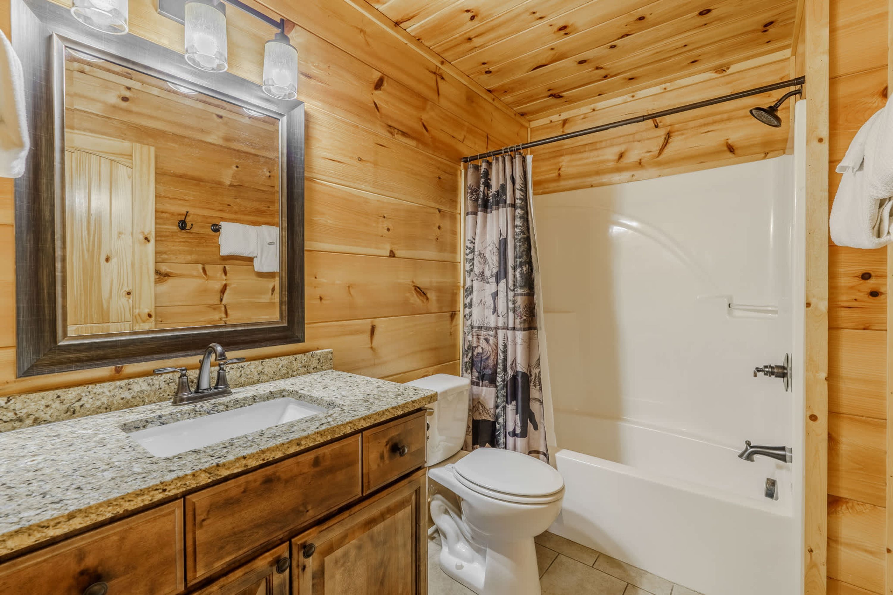 A wooden cabin bathroom with a granite countertop sink, a toilet, a bathtub, and a shower curtain.