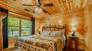 A wooden cabin bedroom with a bed, a ceiling fan, a window, and a nightstand. - Gatlinburg-2brs-hot Tub-arcade Games-fireplace (Gatlinburg)