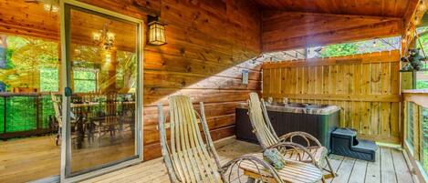 A wooden deck with rustic chairs, a hot tub, and a glass door leading to an outdoor dining area.