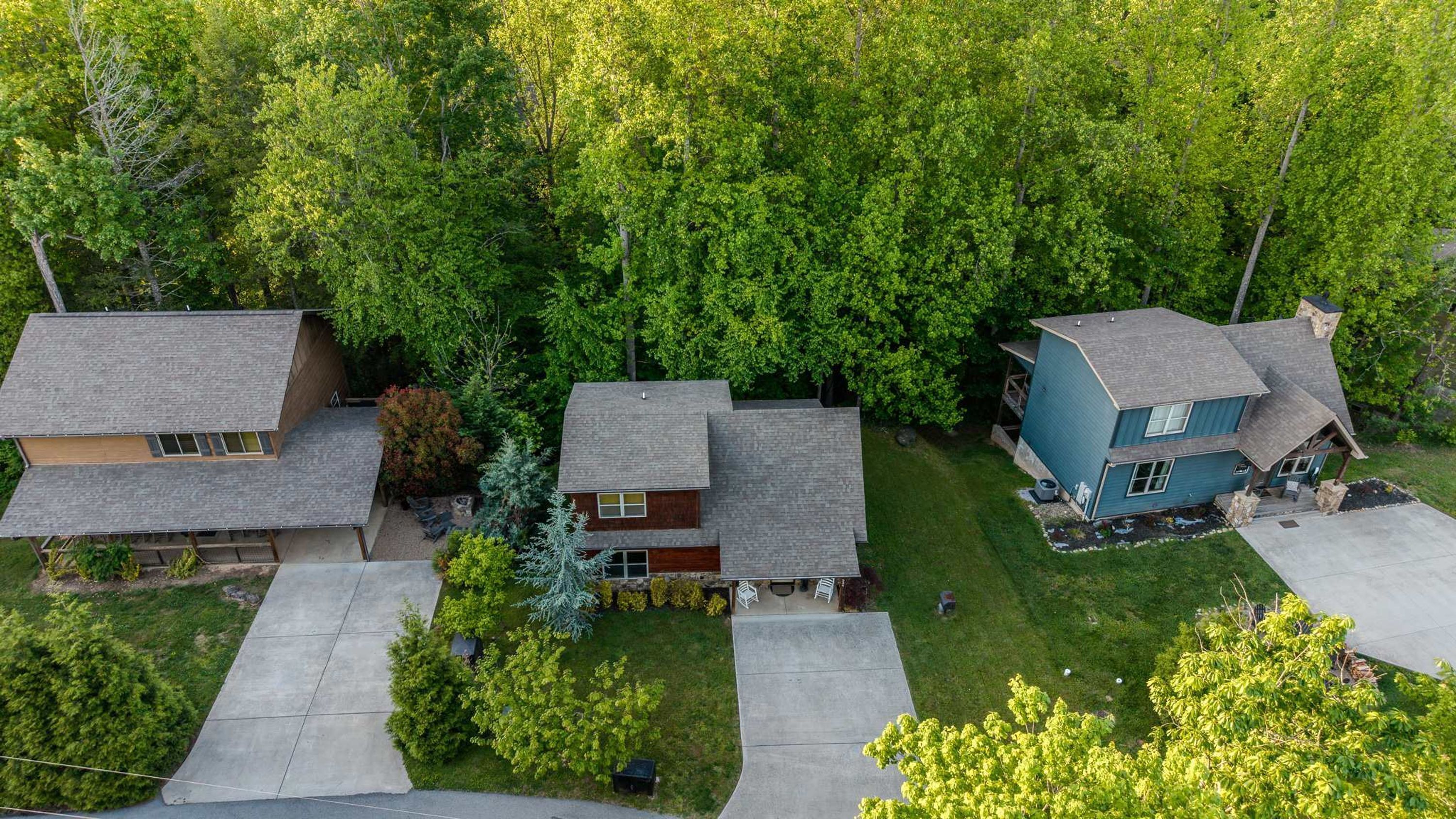 A residential area with three houses, each with a distinct architectural style, surrounded by dense green trees.
