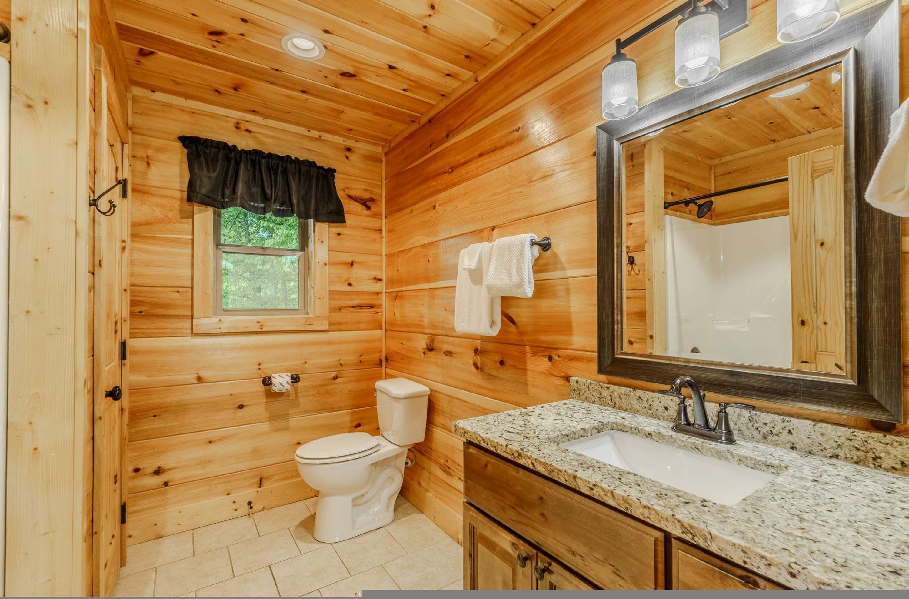 Baño de cabaña de madera con inodoro, lavabo, tocador y un espejo grande.