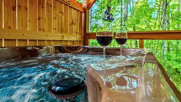 A hot tub with two glasses of red wine, surrounded by wooden walls and a view of greenery. - Gatlinburg-2brs-hot Tub-arcade Games-fireplace (Gatlinburg)