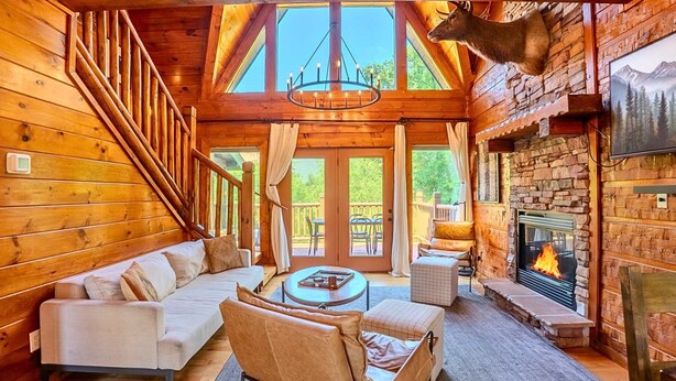 A log cabin interior with a fireplace, wooden walls, a sofa, and a chandelier. - NEW Lux 4 BR Pigeon Forge Dollywood Hot Tub (Pigeon Forge)