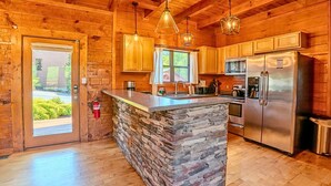 A wooden cabin interior with a stone island, kitchen appliances, and a fire extinguisher. - NEW Lux 4 BR Pigeon Forge Dollywood Hot Tub (Pigeon Forge)