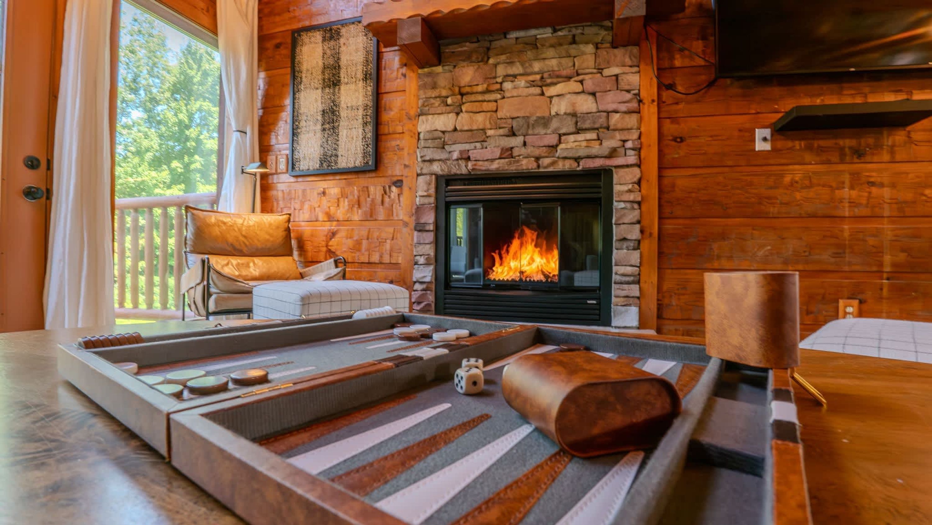 A cozy living room with a stone fireplace, a cushioned seating area, and a view of the outdoors.