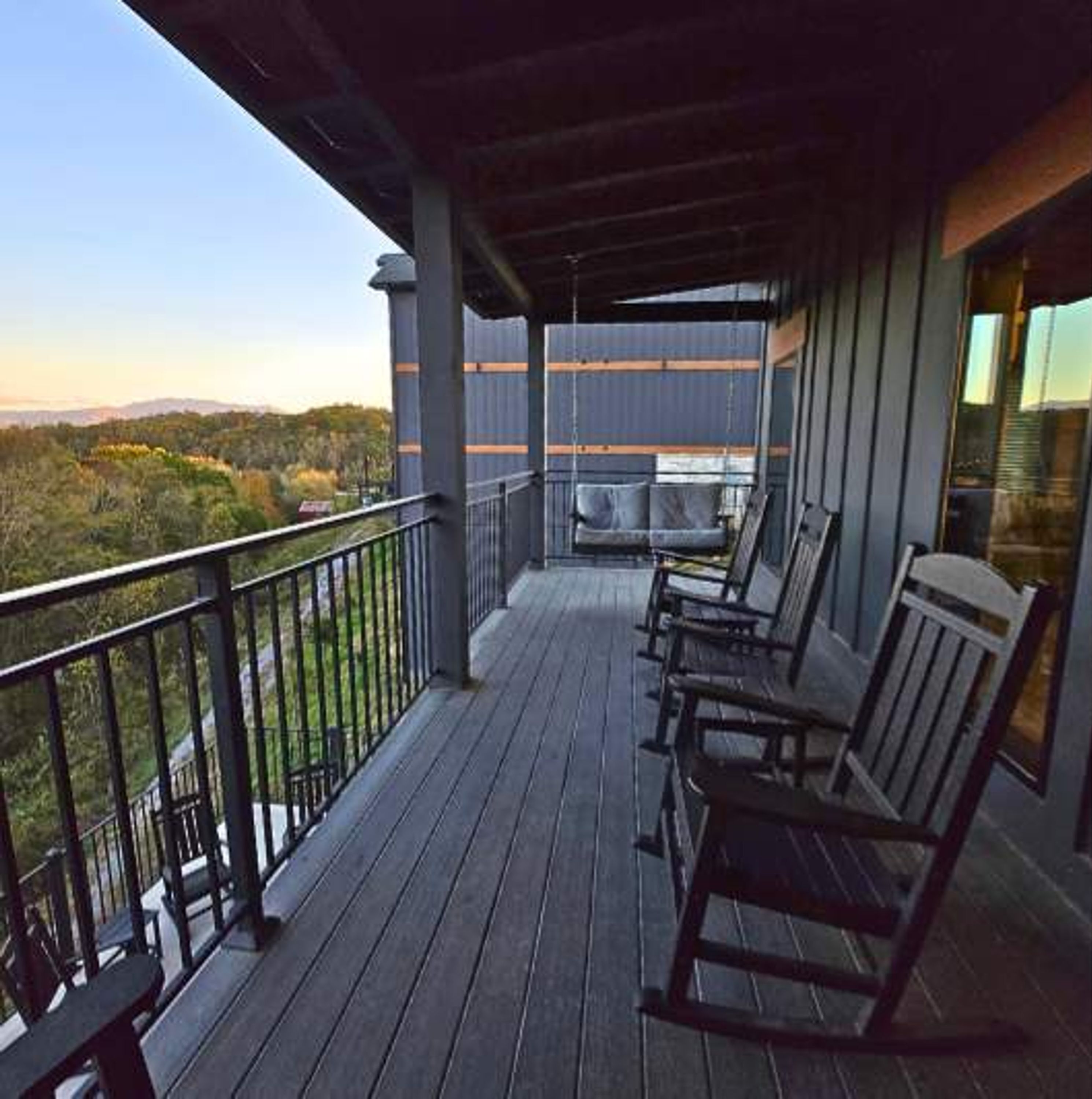 A wooden deck with outdoor furniture, a railing, and a view of the landscape.