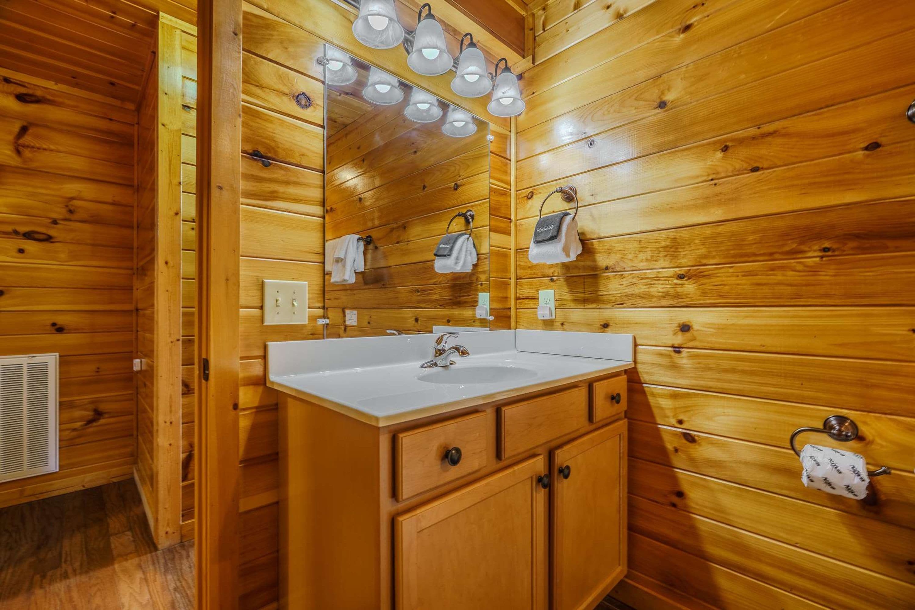 A wooden cabin bathroom with a white sink, wooden cabinets, a mirror, and a towel rack.