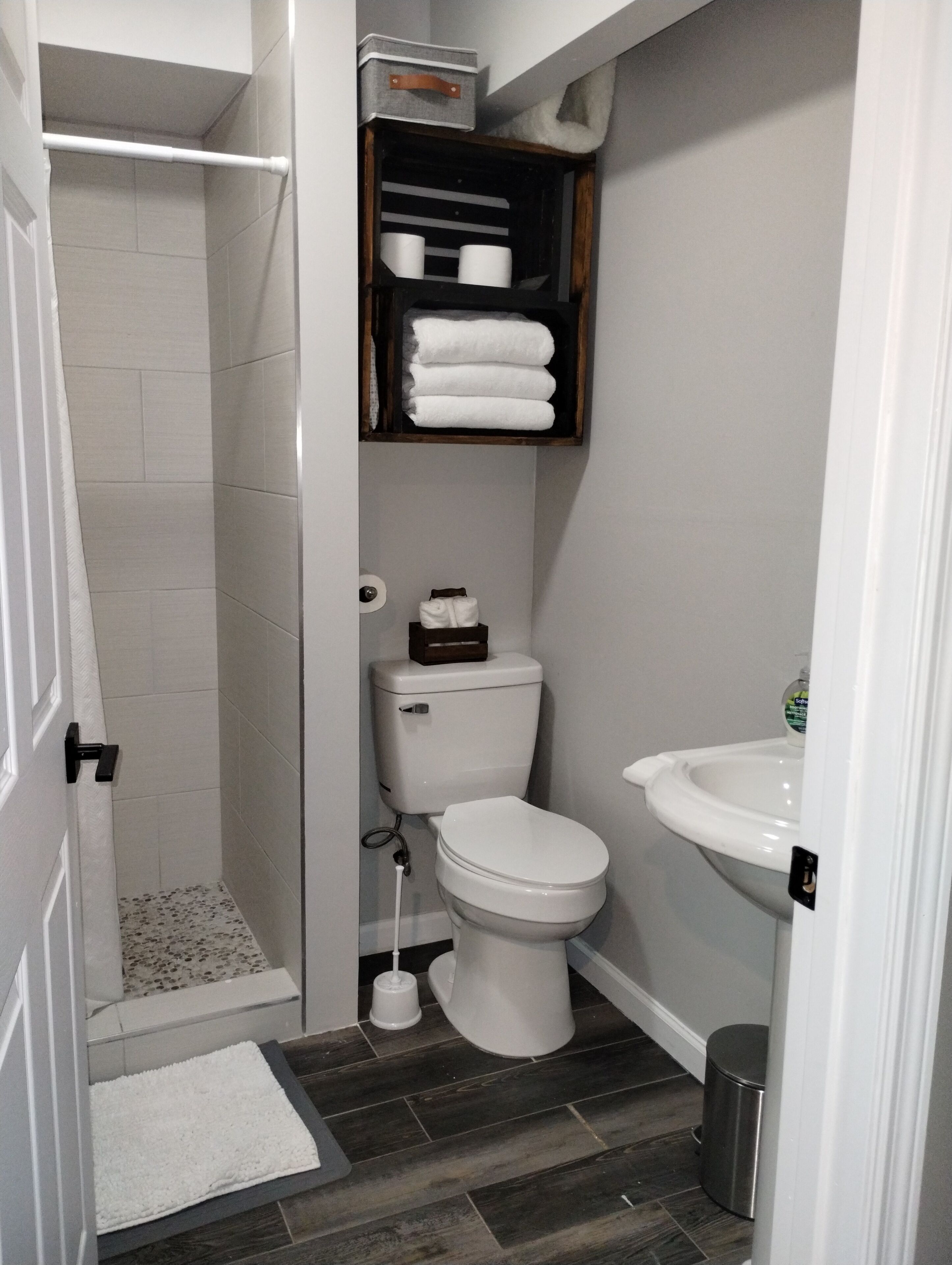 A bathroom with a shower, toilet, sink, and storage shelves.