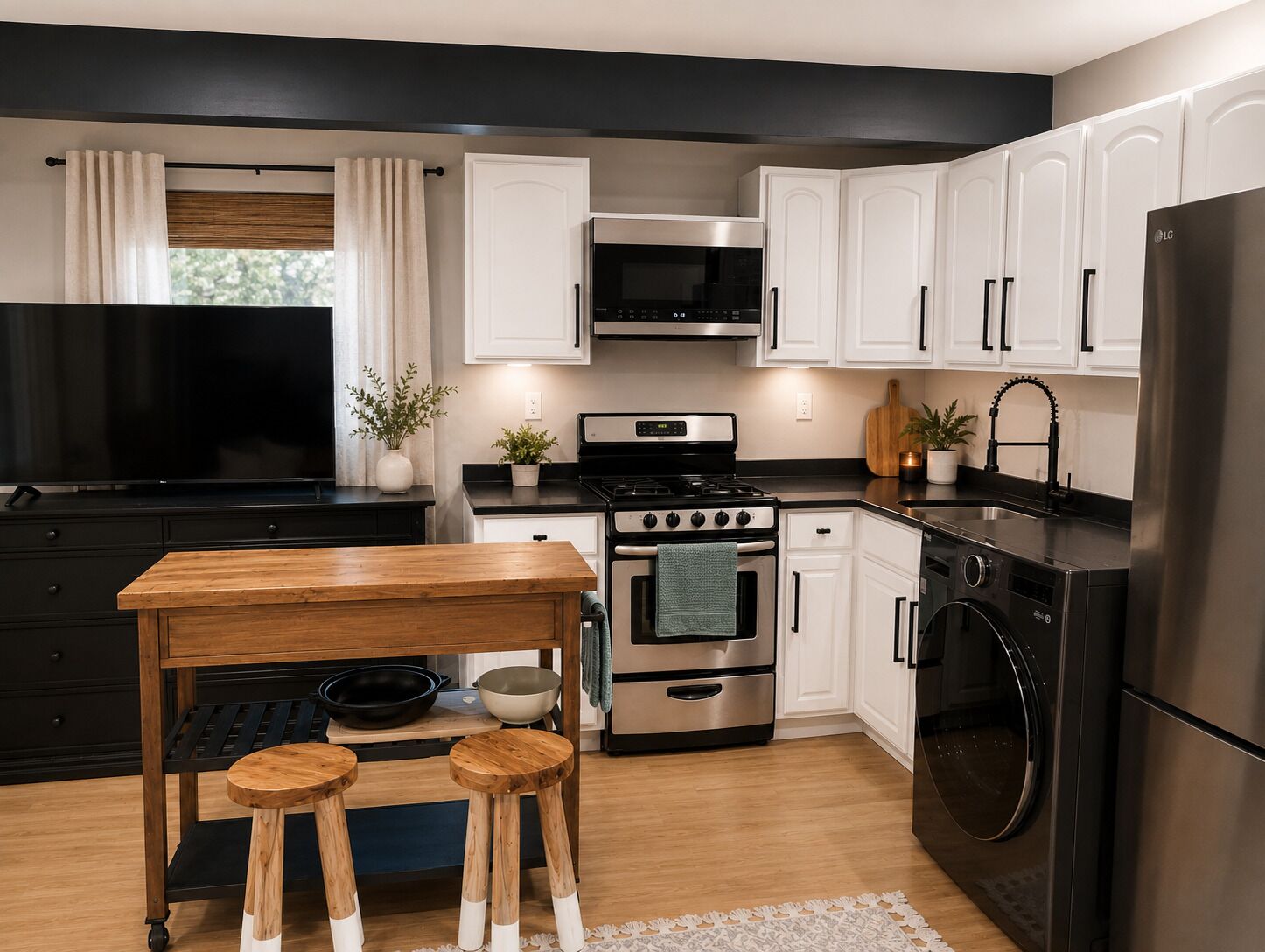 A modern kitchen with white cabinets, stainless steel appliances, a wooden table with stools, and a large window with curtains.