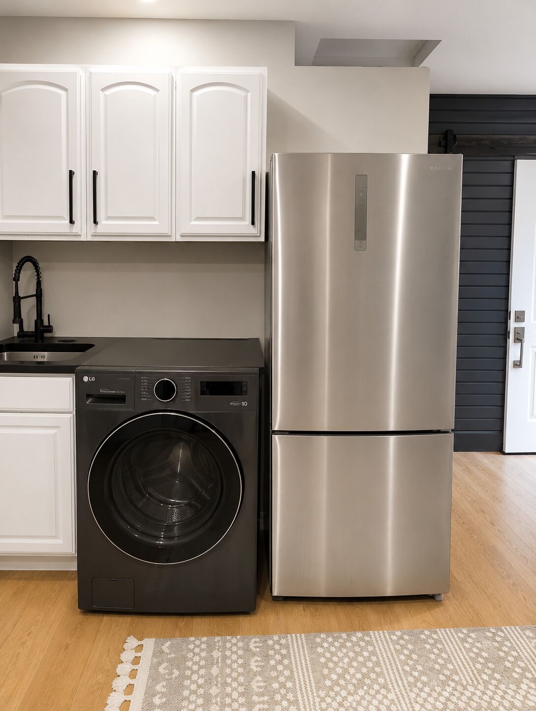 A kitchen with white cabinets, a stainless steel refrigerator, and a black washing machine.