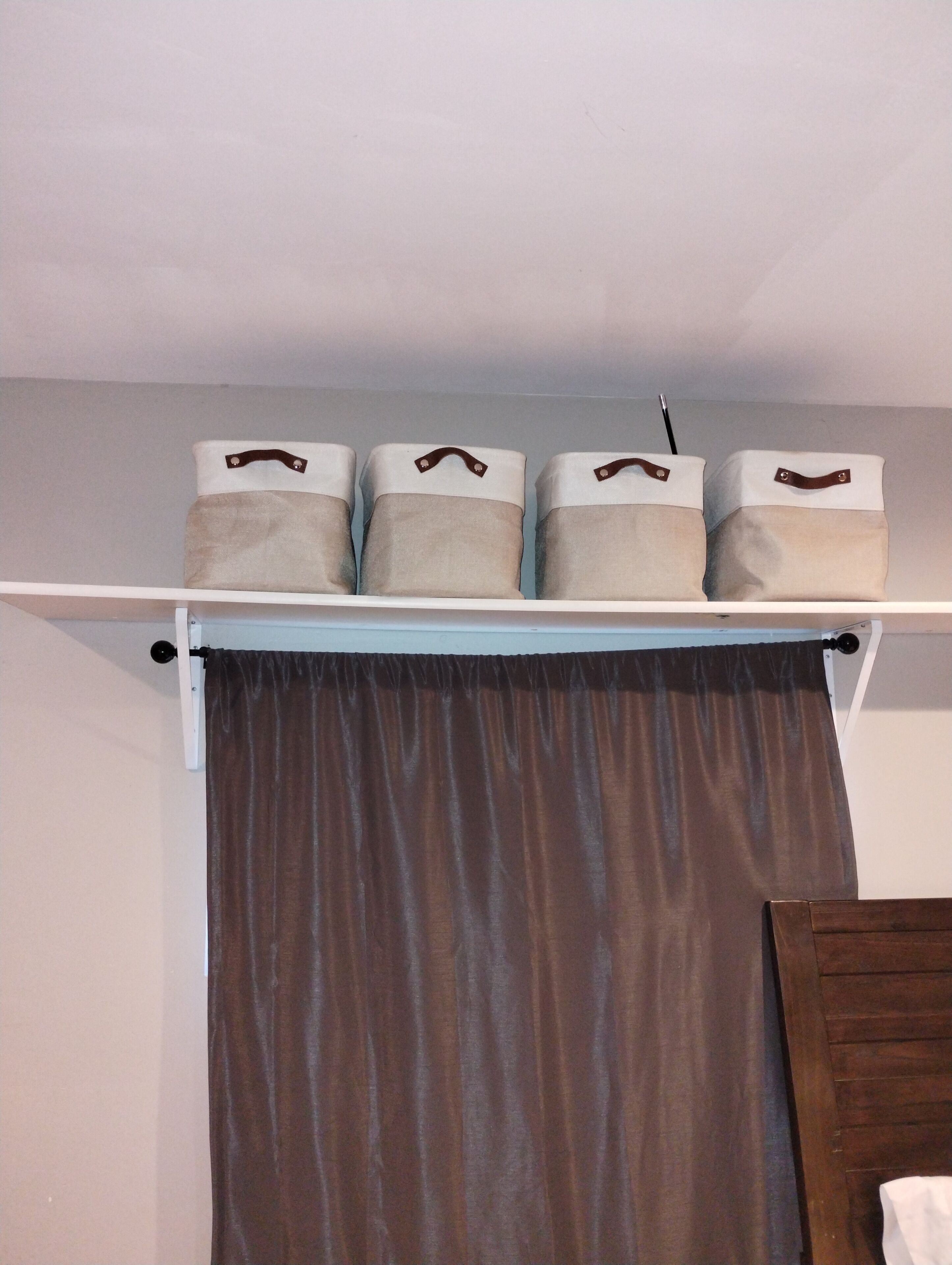 A white shelf with three storage boxes and a brown curtain.