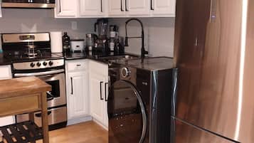 A modern kitchen with stainless steel appliances, white cabinetry, and a wooden dining table.