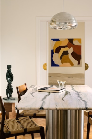 Ein Essbereich mit einem Marmortisch, gewobenen Stühlen, einer modernen Pendelleuchte und abstrakter Kunst an der Wand.