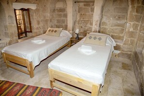 Two wooden beds with white linens, a stone wall, and a wooden nightstand with a lamp. - NAHIL MİSAFİREVİ MARDİN (ARTUKLU)