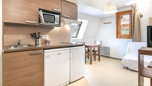 A compact kitchen with a microwave, dishwasher, and a dining area with a table and chairs. - Studio Near Vercors Regional Nature Park (Gresse-en-Vercors)