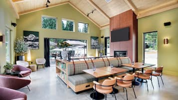Un interior moderno con techo alto, vigas de madera, un área de descanso con sofá y sillones, chimenea y ventanas amplias.