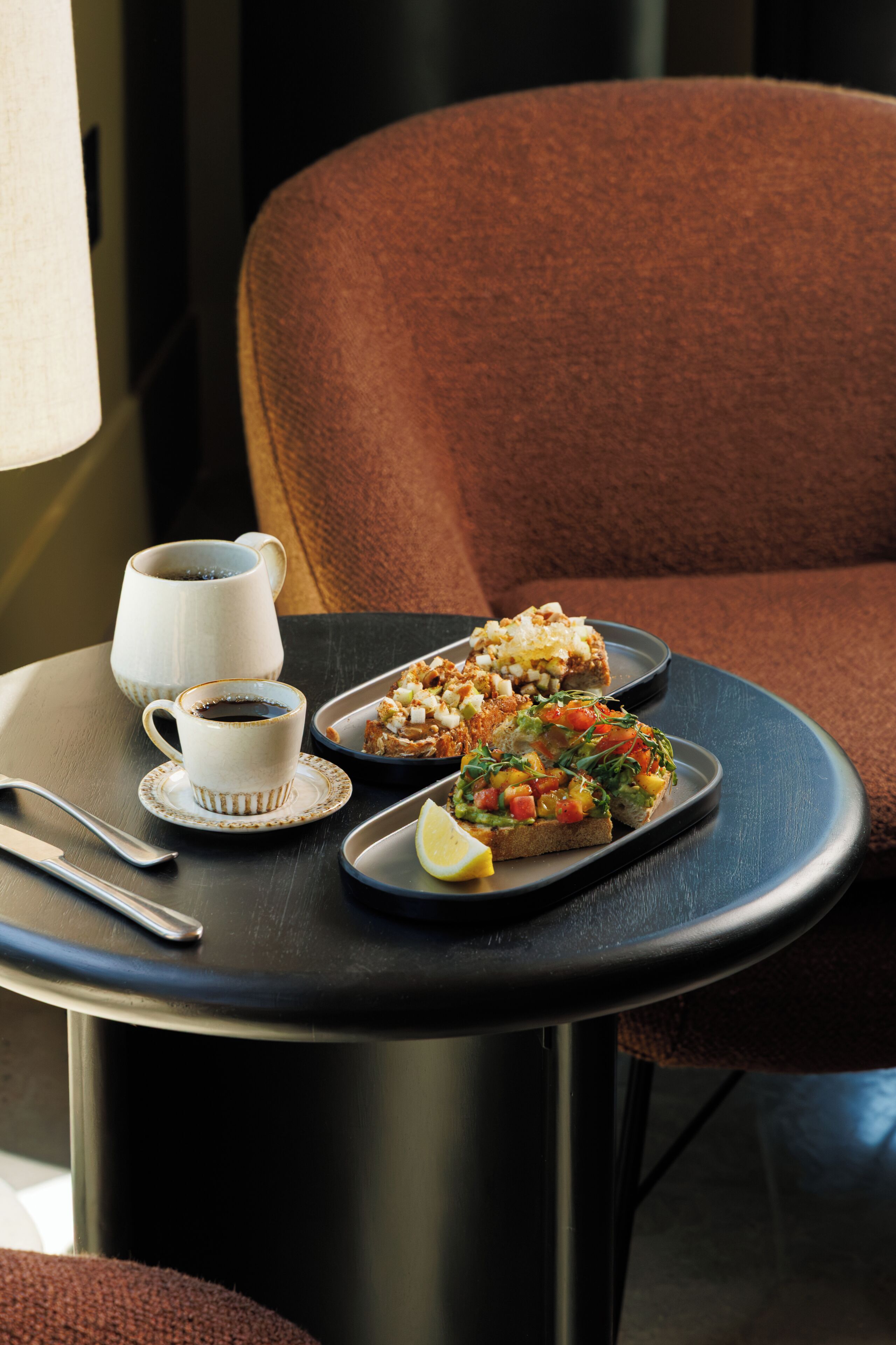 Une table avec une tasse de café, deux assiettes de nourriture et une tranche de citron.