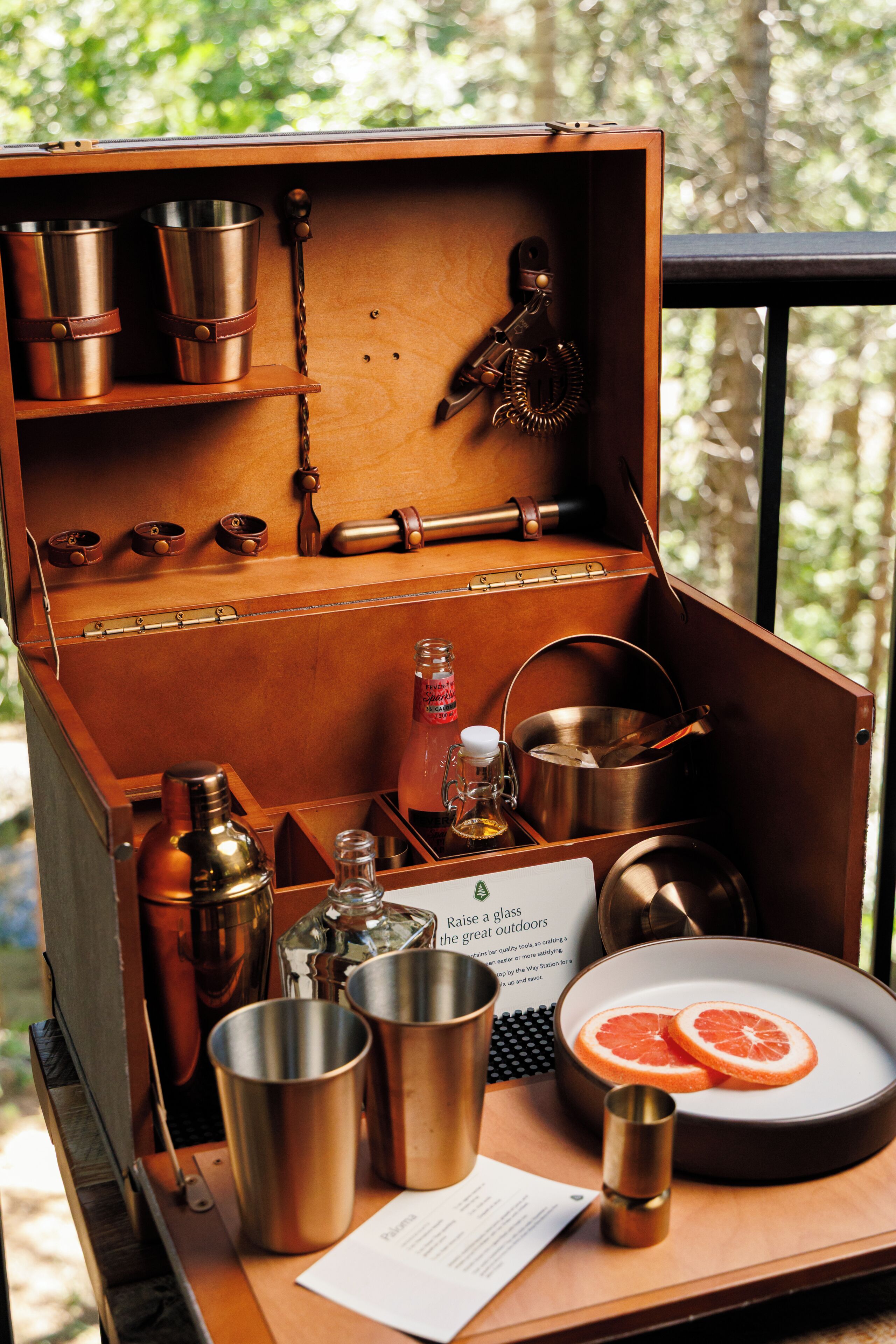 A wooden box with various metal containers and utensils, a glass bottle, and a plate with fruit slices.