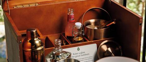 A wooden box with various metal containers and utensils, a glass bottle, and a plate with fruit slices.