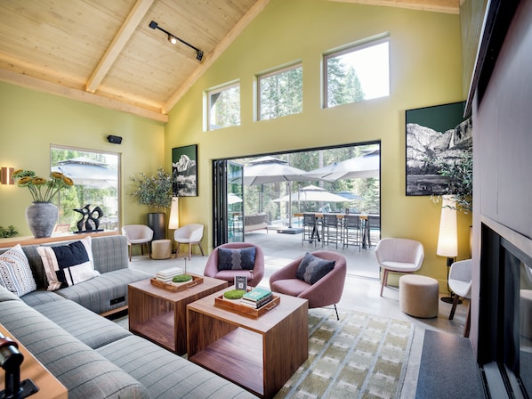 A modern living room with a sofa, armchairs, a coffee table, and a dining area with outdoor umbrellas. - Waybound Yosemite (Fish Camp)