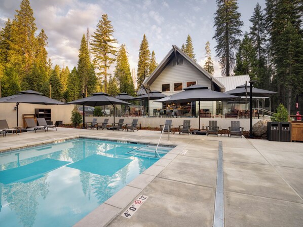 A pool area with lounge chairs and umbrellas, surrounded by tall trees.