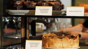 Una vitrina con varios productos de panadería y pastelería, incluyendo un muffin de arándanos y quiche de espárragos y gruyer.